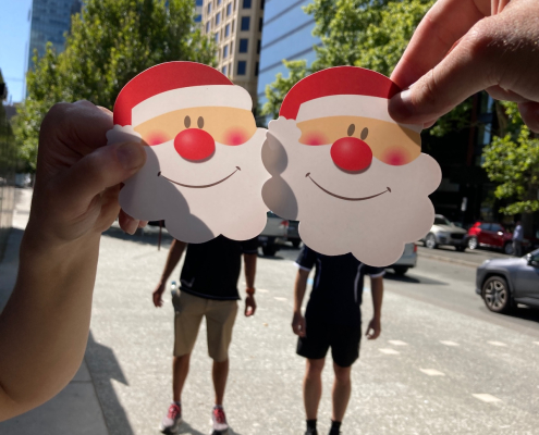 Hands holding Santa face cutouts during a Christmas scavenger hunt on the Gold Coast city streets.