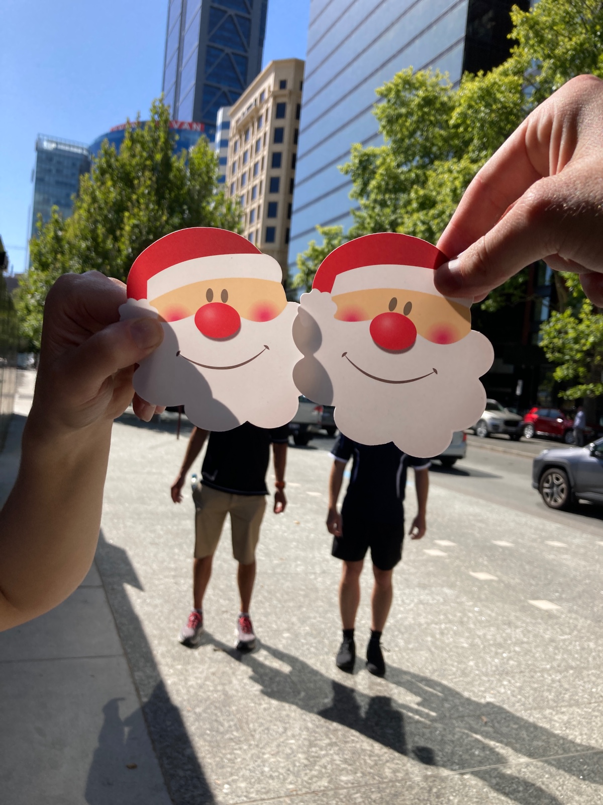 Hands holding Santa face cutouts during a Christmas scavenger hunt on the Gold Coast city streets.
